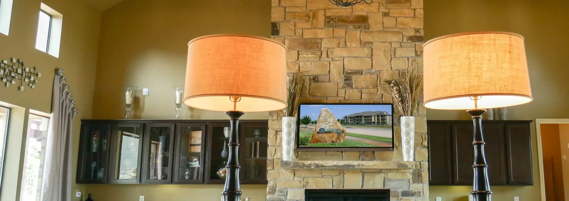 a large stone fireplace with two lamps and a television at The Anatole on MacArthur North