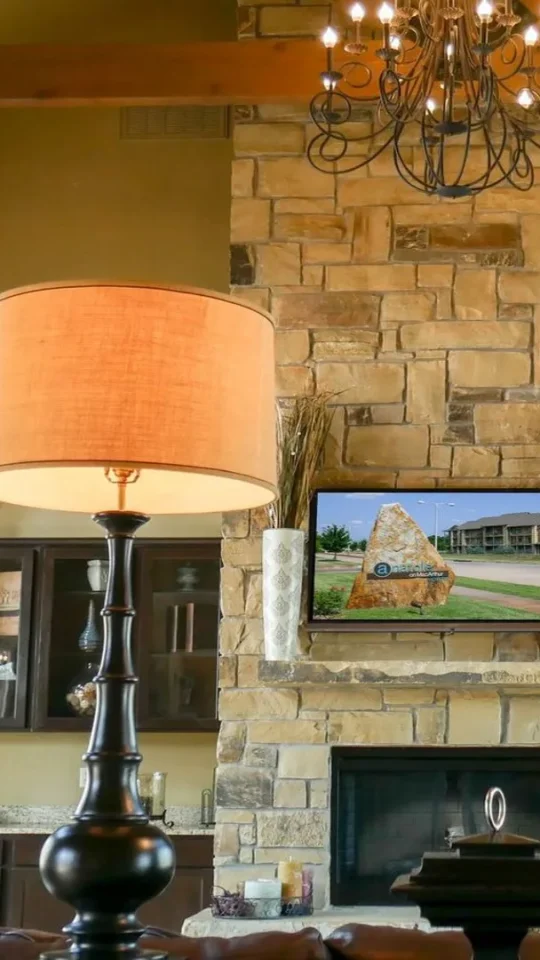 a large stone fireplace with two lamps and a television at The Anatole on MacArthur North